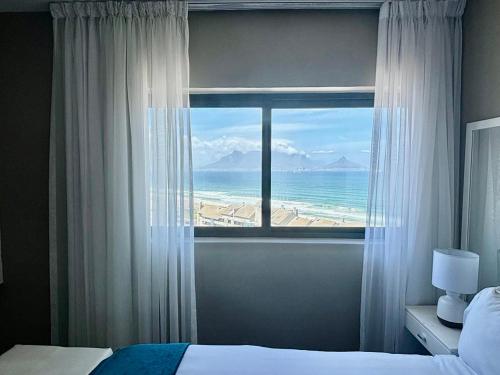 a bedroom with a window with a view of the ocean at Relaxing Blouberg Beachfront view Apartment in Cape Town