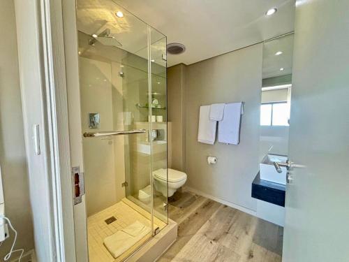 a bathroom with a toilet and a glass shower at Relaxing Blouberg Beachfront view Apartment in Cape Town