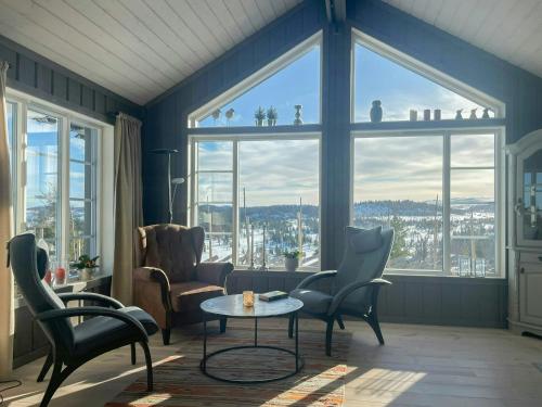 a living room with chairs and a table and large windows at Cabin With Panoramic Views Over The Mountains in Nesbyen