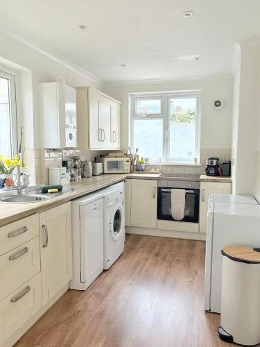 a kitchen with white cabinets and a washer and dryer at Beach Walk Cottage in Walton-on-the-Naze