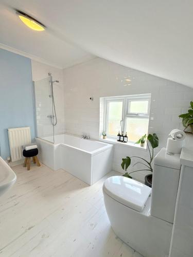 a white bathroom with a tub and a toilet at Beach Walk Cottage in Walton-on-the-Naze