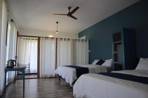 a bedroom with two beds and a ceiling fan at Rakas Guest House Ooty in Ketti