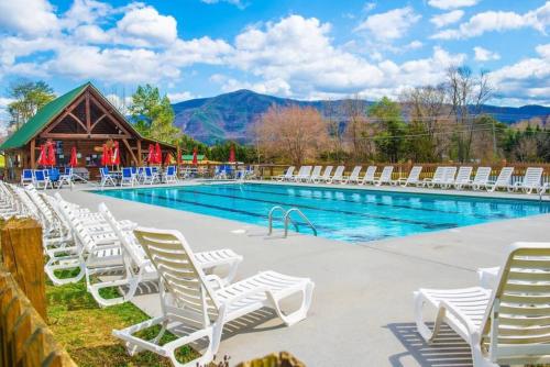 a swimming pool with white chairs and a cabin at Bearfoot Pines - True Log Cabin - Wi-Fi, Hot Tub, Fishing, Deck with views! - Mins to PF in Sevierville