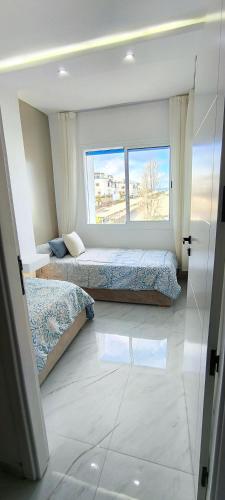 two beds in a room with a large window at Magnifique appartement de trois chambres, Résidence Kabila Vista in M'diq