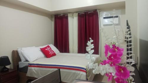 a small bed in a room with red curtains and flowers at B4B Staycation Avida Aspira in Cagayan de Oro