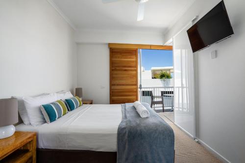 a bedroom with a bed and a tv and a balcony at Rolling Surf Resort in Caloundra