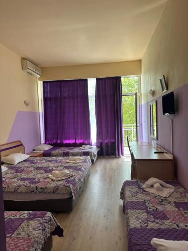 a hotel room with three beds and purple curtains at Hotel RIVA in Golden Sands