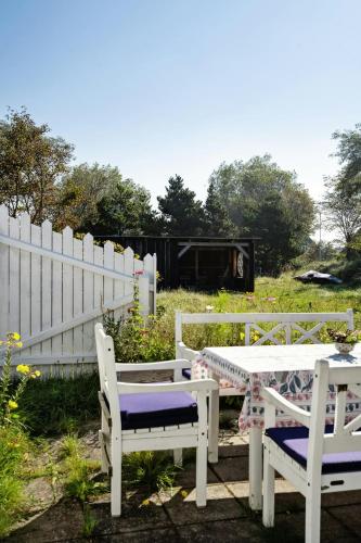 two white benches and a table and a fence at Charming Tiny House In Sønderho in Fanø