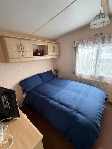 a bedroom with a blue bed and a window at seton sands caravan in Port Seton