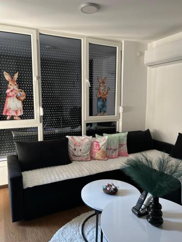 a living room with a black couch and two windows at Mirror Apartments in Petrovec