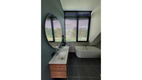 a bathroom with a sink and a tub and a mirror at De Bosanemoon with Sauna | 6 persons in Gasselte