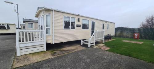 a white tiny house with a porch and a white gate at Towyn Happy Days S7 in Rowen