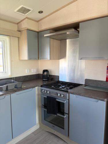 a kitchen with a stove and white cabinets at PG177 Golden Palm Resort 8 Berth Caravan With Decking in Chapel Saint Leonards