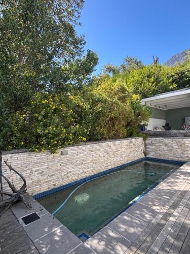 a swimming pool next to a brick wall and trees at 1 Fountain private pool in Hout Bay