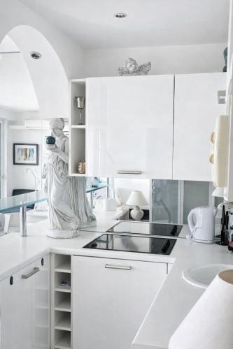 a white kitchen with white cabinets and a statue at Le Reflet d'Azur - les pieds dans l'eau in Antibes