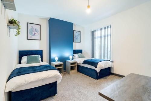 a bedroom with two beds and a blue wall at Spacious 3BR Stay - Free Parking - Near City Centre - Sleeps 6 in Manchester