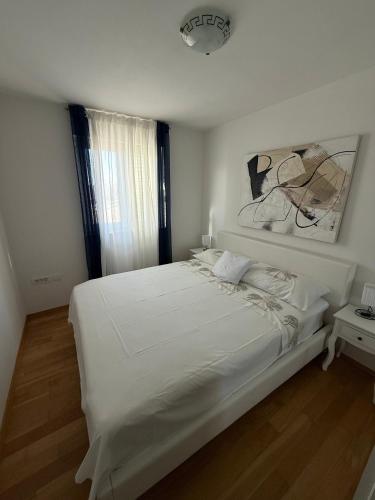 a white bedroom with a large white bed and a window at Apartment Perla in Dinjiška