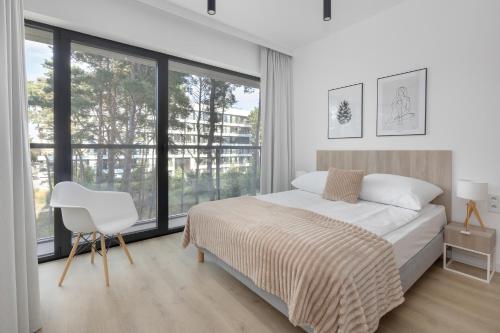 a white bedroom with a bed and a white chair at Shellter Resort Apartment by Solarento in Rogowo