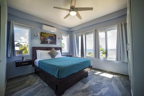 a bedroom with a bed with a ceiling fan and windows at Villa Armoniosa Ocean View 2BR w/ Beachfront Pool - Upper Level in Placencia