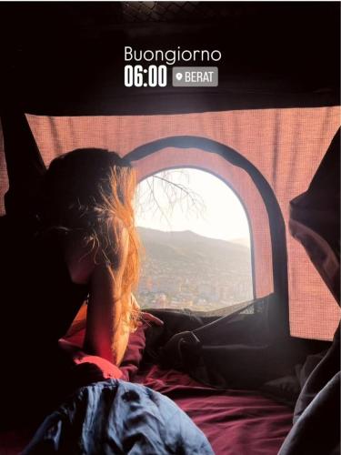 a woman laying on a bed looking out a window at 4x4 RoofTent Camper Offroad in Tirana