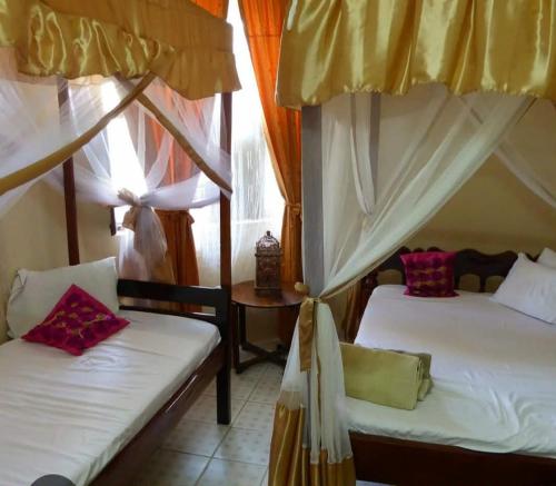 a bedroom with two beds and a table with a window at Manch Lodge Vuga Zanzibar in Zanzibar City
