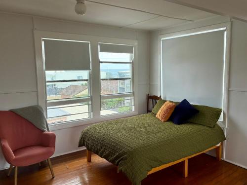 a bedroom with a bed with a chair and two windows at Peach Me Beach Shack in Boat Harbour