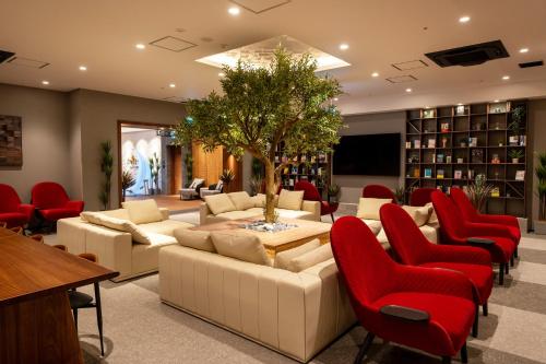 a living room with couches and red chairs and a tree at Kanohotel and Cabin Chiba Soga in Chiba