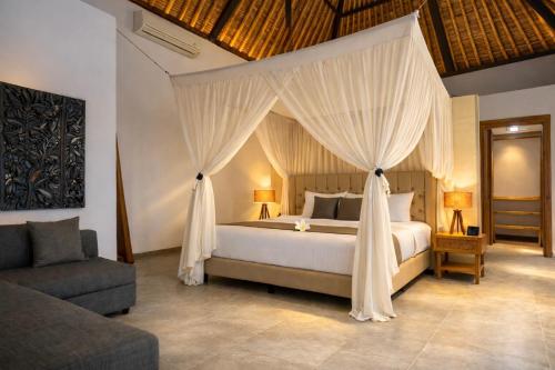 a bedroom with a canopy bed with a chair and a couch at Balidroomvilla's in Candidasa