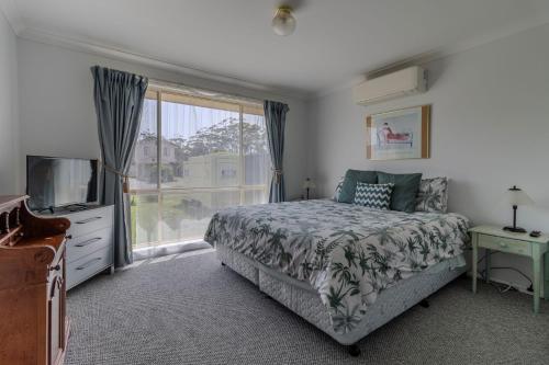 a bedroom with a bed and a tv and a window at Holiday on the Water in Sussex Inlet