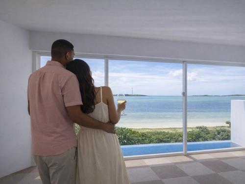 a man and woman looking out a window at the ocean at VOYAN Resort MiyakojimaーAZOMARE アゾマーレ in Miyako-jima