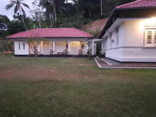 a white house with a red roof and a yard at George Bungloaw in Henegama