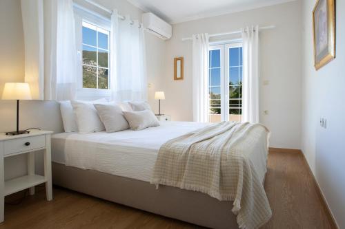 a white bedroom with a bed and two windows at Villa Morris in Nydri