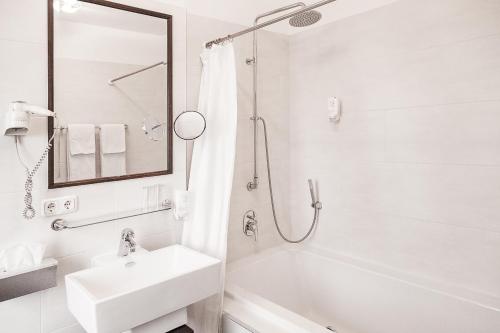 a white bathroom with a sink and a bath tub at Hotel Aviv Dresden in Dresden