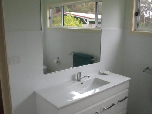a white bathroom with a sink and a mirror at Bournda Retreat in Merimbula