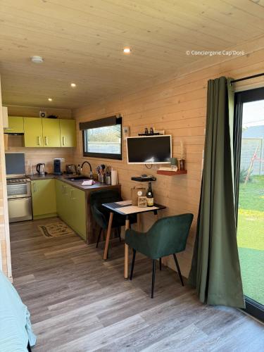 a kitchen in a tiny house with a table and a tv at La Roulotte - Tiny House 150m de la Plage in Portbail