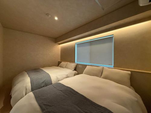two beds in a small room with a window at Ishiki by b hotel - Next to Station Newly Renovated 3BR with Island Kitchen in Hiroshima