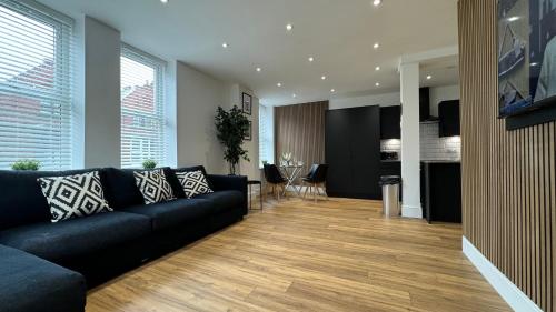 a living room with a black couch and a kitchen at Stylish 2 Bedroom Coastal Apartment near Crosby Beach & Liverpool in Waterloo