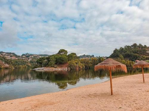 two straw umbrellas on a beach near a body of water at Casa Da Clarinha in Castelo de Paiva