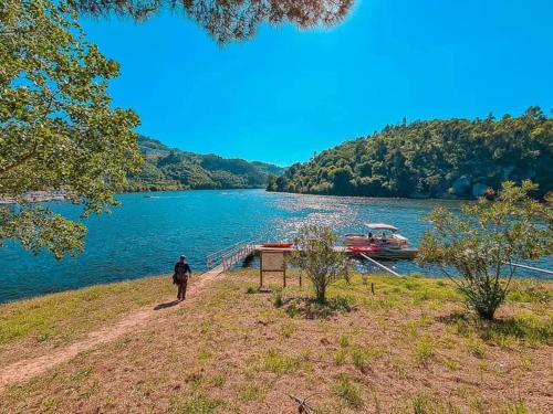 a man walking along the shore of a lake with a boat at Casa Da Clarinha in Castelo de Paiva
