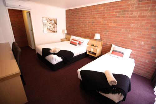 a room with two beds and a brick wall at Pevensey Motor Lodge in Echuca