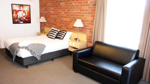 a bedroom with a bed and a leather chair at Pevensey Motor Lodge in Echuca