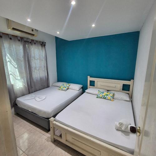 two beds in a room with a blue wall at Hostal Casa del Palmar in Santa Marta
