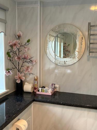 a bathroom with a sink with a mirror and flowers at All Seasons Bed & Breakfast - Adults Only in Weston-super-Mare