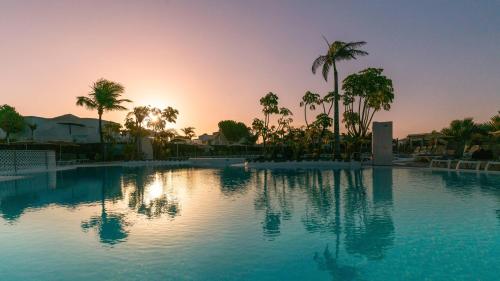a swimming pool with palm trees and a sunset at BLUESEA Alyssa Suite Hotel in Playa Blanca