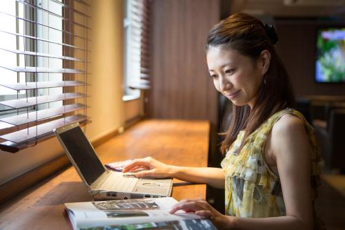 a woman sitting at a table using a laptop computer at Shinjuku Kuyakusho-mae Capsule Hotel in Tokyo