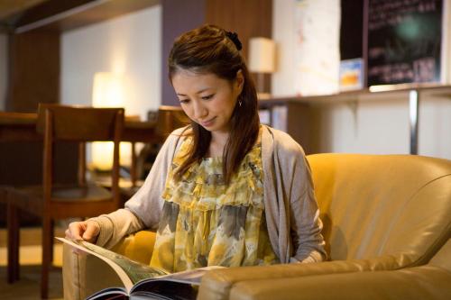a woman sitting in a chair reading a book at Shinjuku Kuyakusho-mae Capsule Hotel in Tokyo