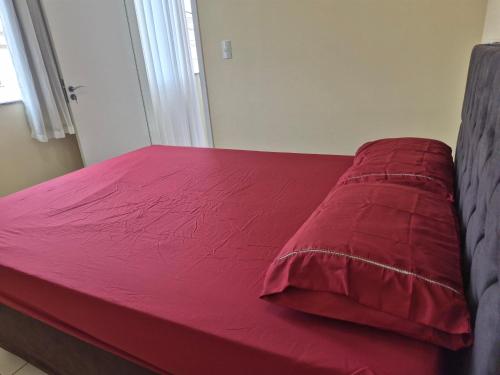 a red bed with a red pillow on it at AP Climatizado aconchego com Mercado em frente in Vitória da Conquista