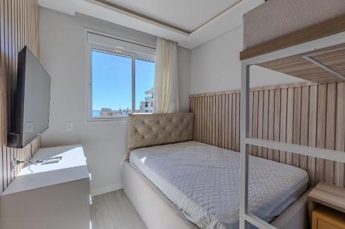 a bedroom with a bunk bed with a desk and a television at Apartamento 2 suítes C/Piscina in Bombinhas