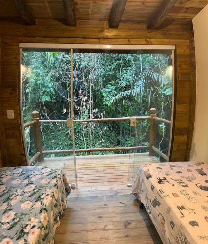 two beds in a room with a large window at Chalé Shangri-la in Paraty