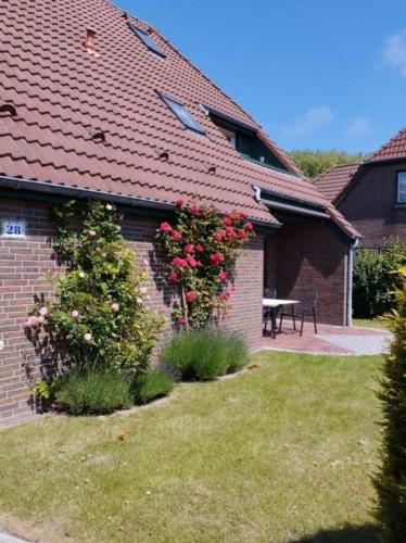 a house with a red roof with a table and flowers at lüttje Meerzeithuus in Carolinensiel